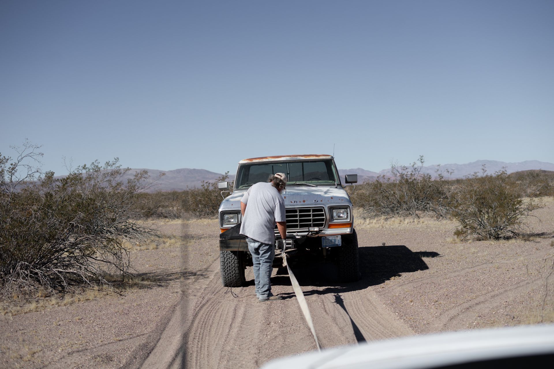 A driver stopped beside a broken-down pickup on an empty desert road