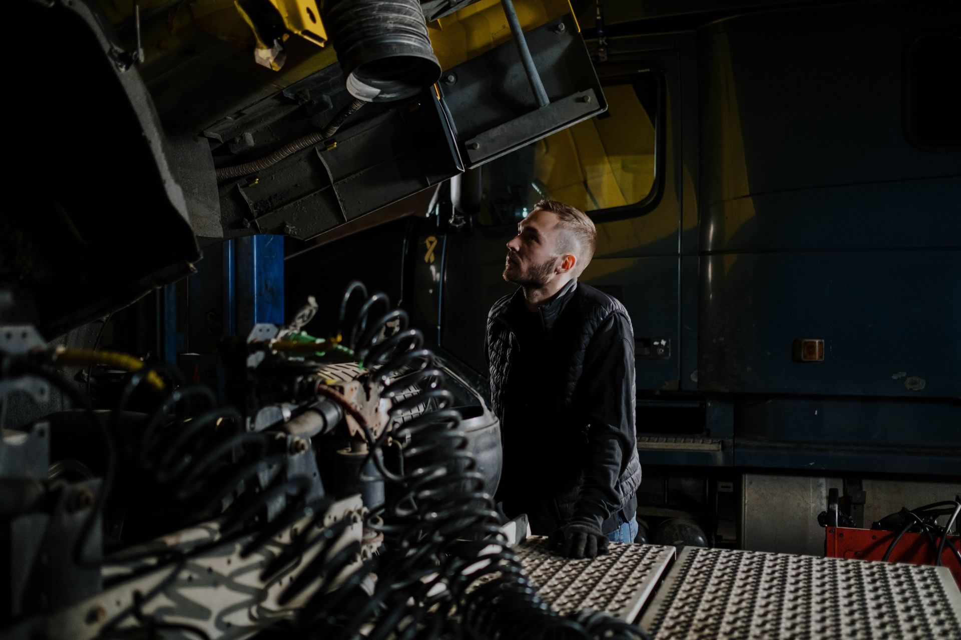 A technician leaning into an open truck engine bay with a work light