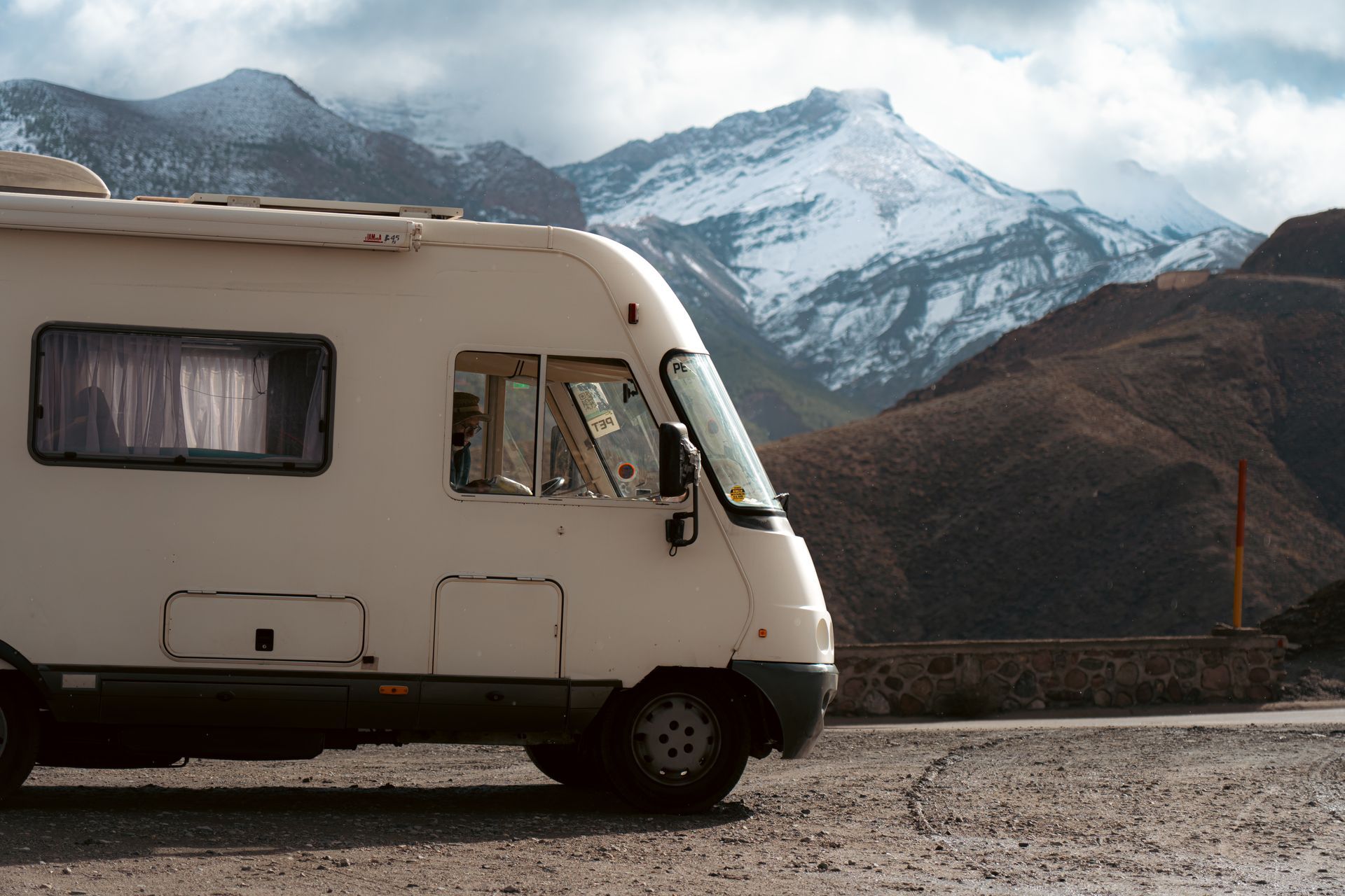 A motorhome parked at the roadside with snow-capped mountains behind it