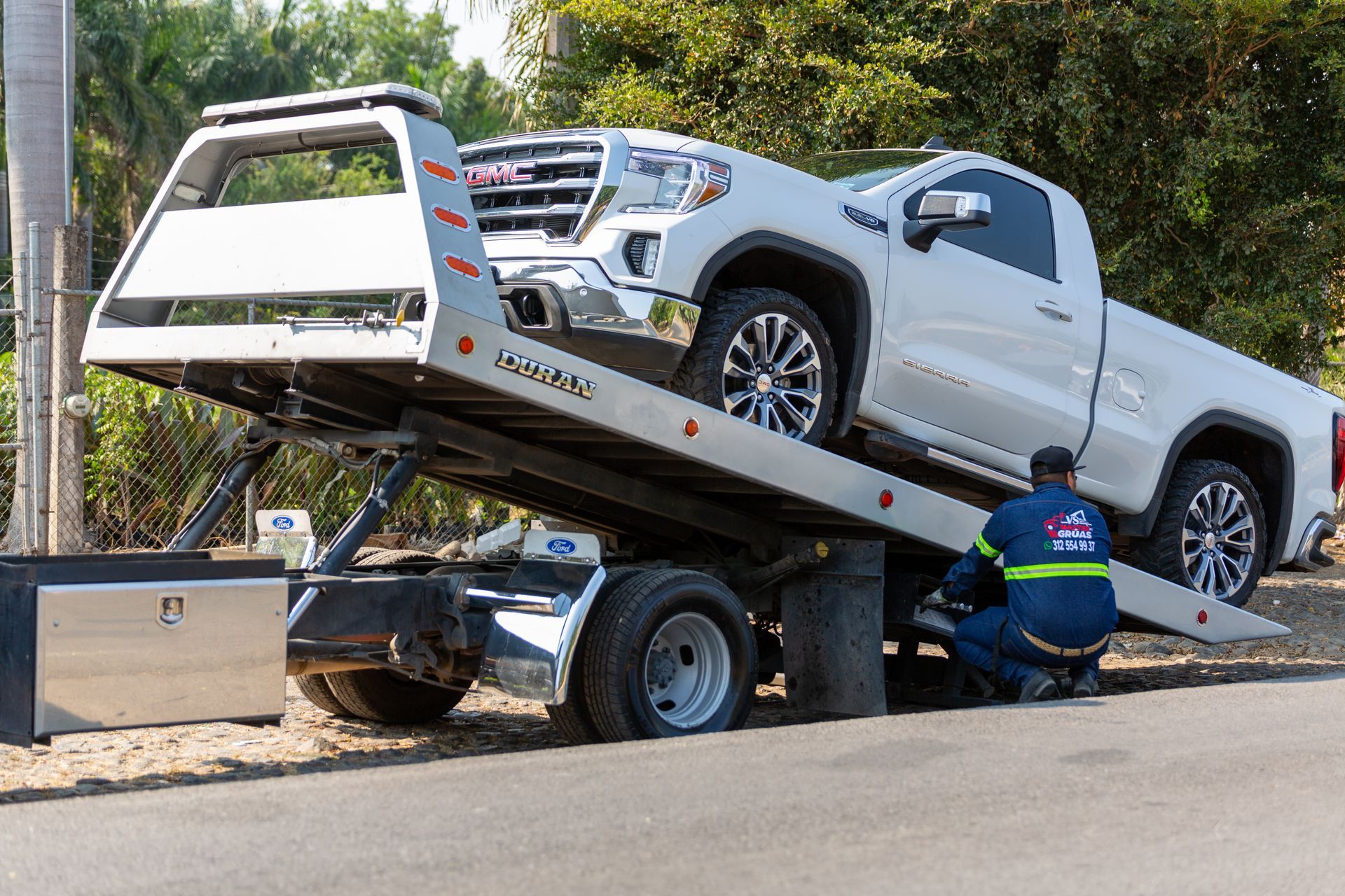 A tow truck operator winching a pickup onto the deck at the roadside